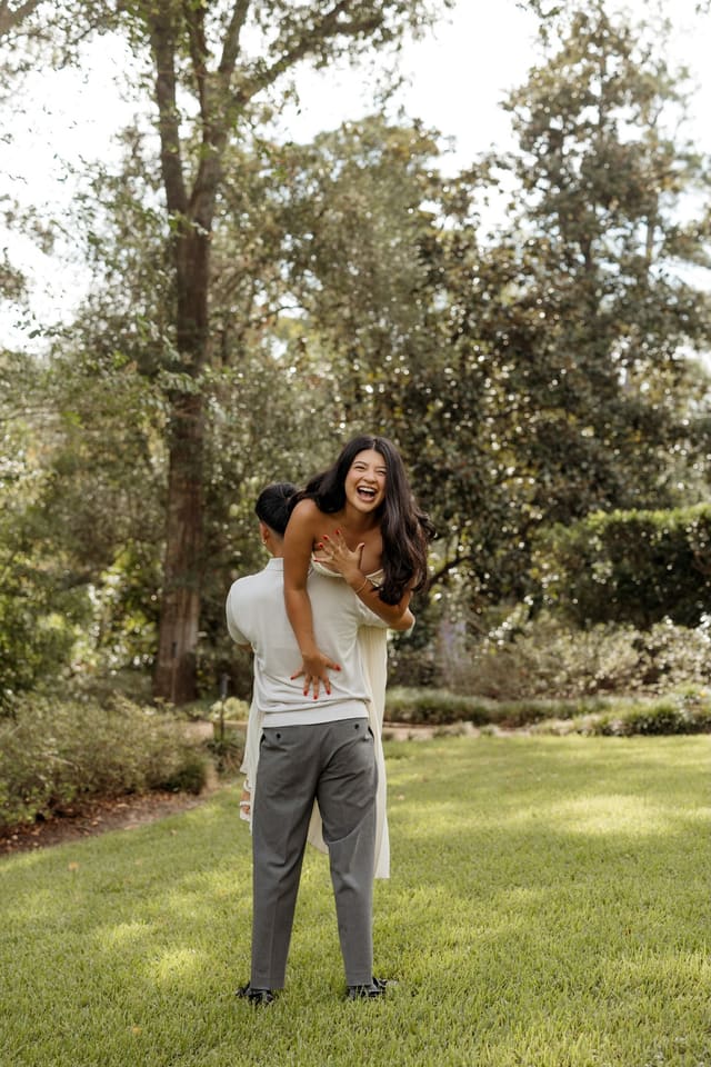 Genesis laughing as Julian carries her on his back across a lawn